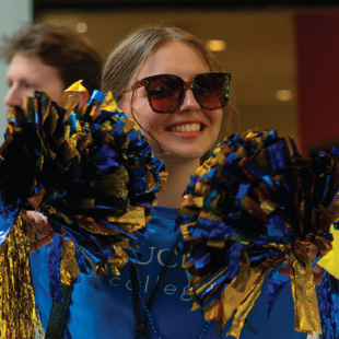 Am alum wearing a Goucher t-shirt, sunglasses and waving pom-poms during the Alumni Weekend Pep Rally.