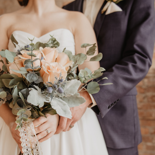 wedding bouquet held by bride with groom behind