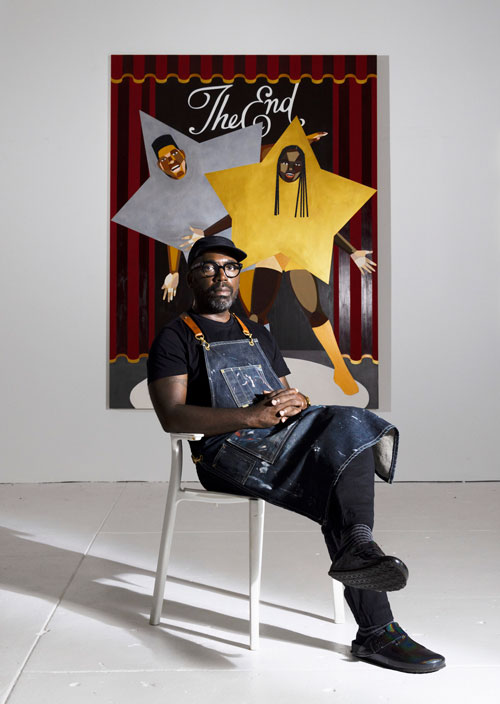 Derrick Adams sitting infront of his exhibition pieces.
